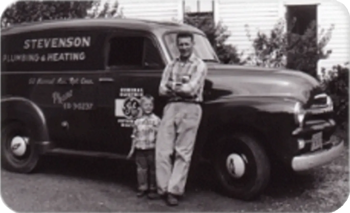 Man and child stand by a Stevenson Plumbing & Heating work van. Black and white photo.