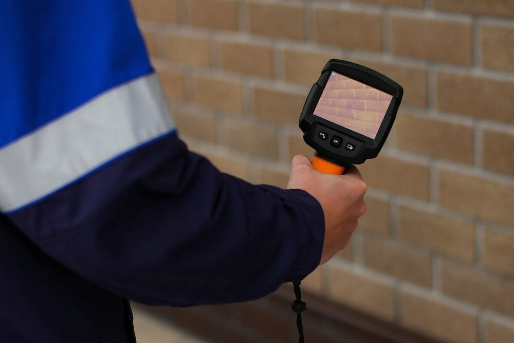 Person in Workwear Holds a Digital Inspection Camera Against a Brick Wall — AD Plumbing & Maintenance in Nicholls, ACT