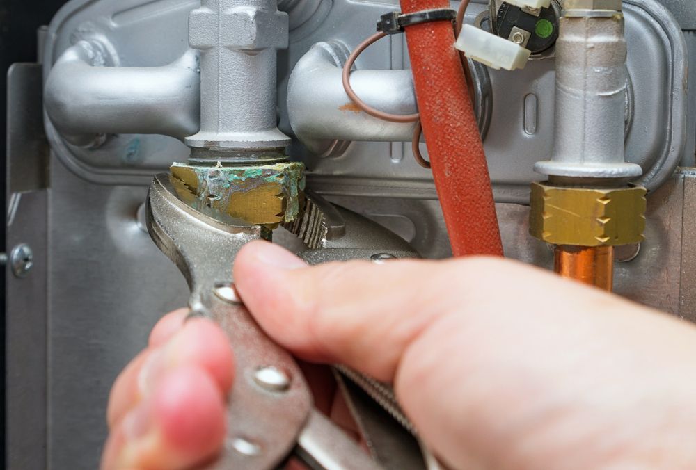 Person Tightening a Pipe Fitting With Pliers on a Metal Plumbing Assembly — AD Plumbing & Maintenance in Canberra, ACT