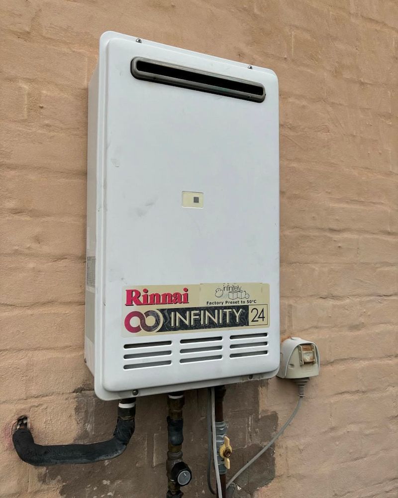 White Rinnai Infinity 24 Tankless Water Heater Mounted on a Brick Wall — AD Plumbing & Maintenance in Nicholls, ACT