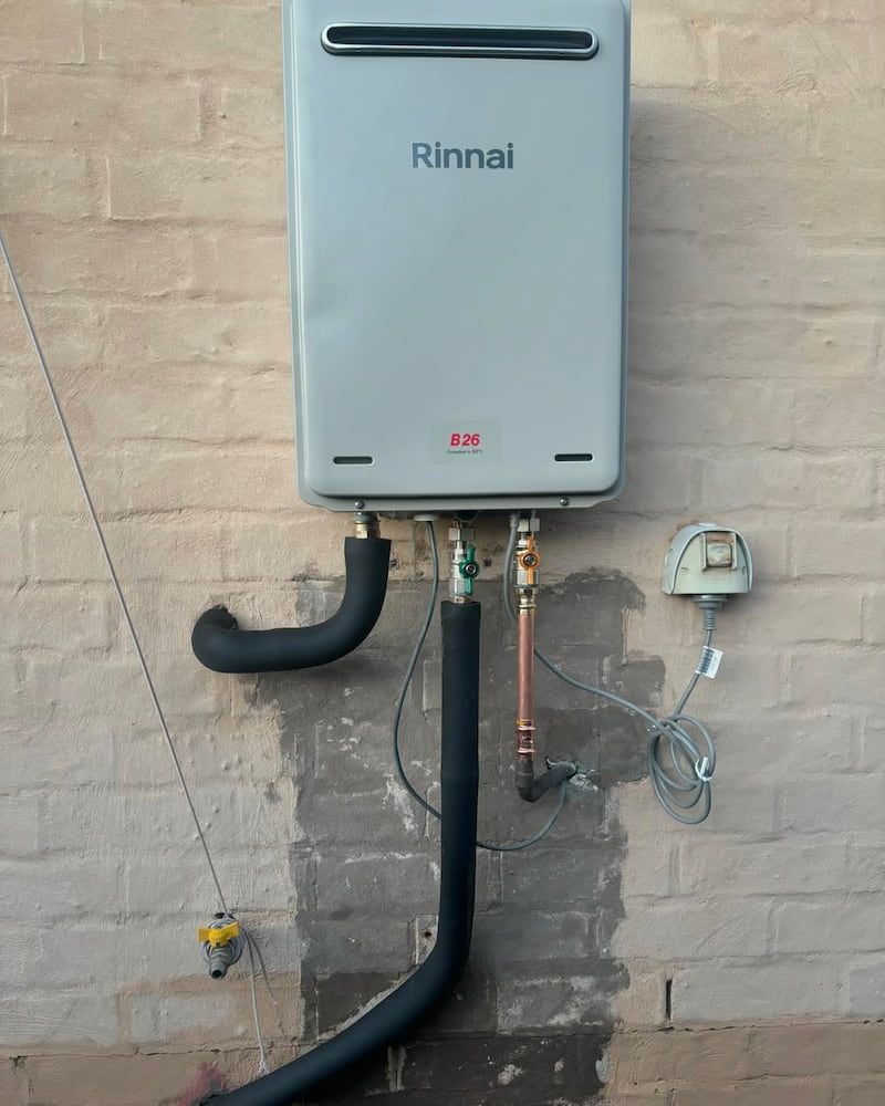 Rinnai Tankless Water Heater Mounted on a Brick Wall, With Black Insulated Pipes — AD Plumbing & Maintenance in Nicholls, ACT