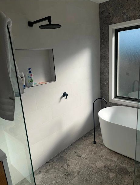 Modern Bathroom With a White Tub, Showerhead, and a Window — AD Plumbing & Maintenance in Nicholls, ACT