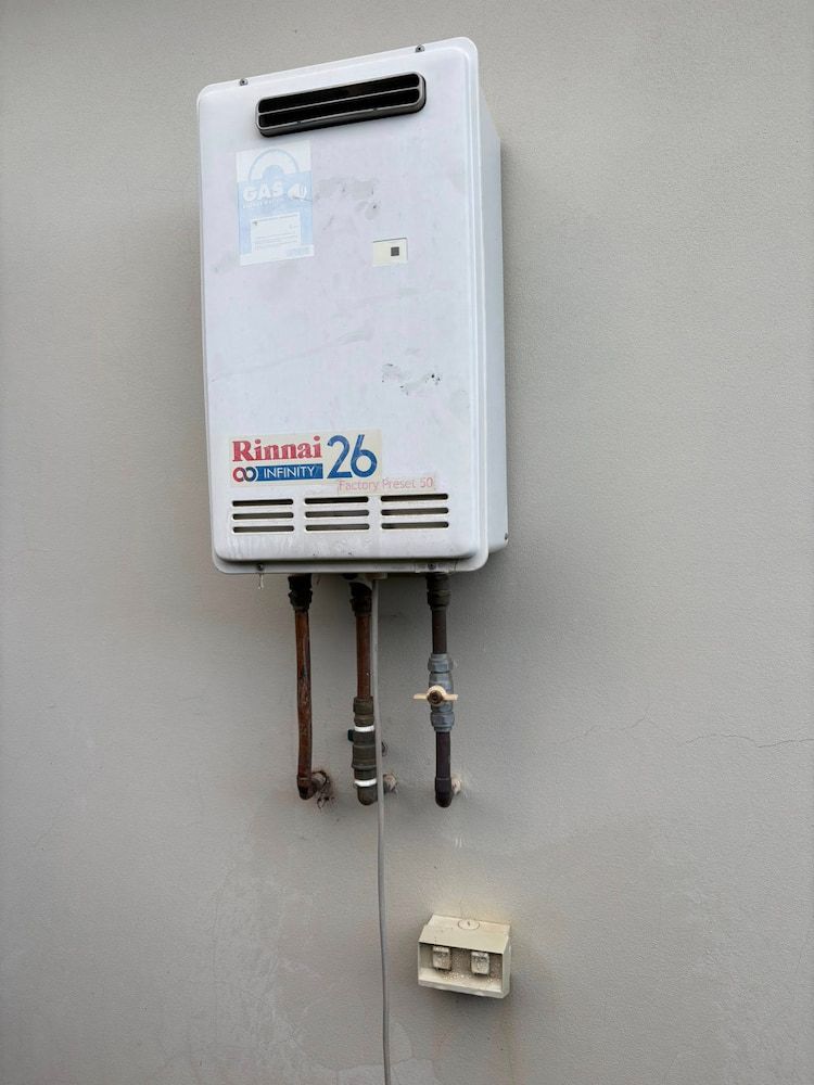 Rinnai 26 Tankless Water Heater Mounted on a Gray Wall With Copper Pipes Below — AD Plumbing & Maintenance in Nicholls, ACT