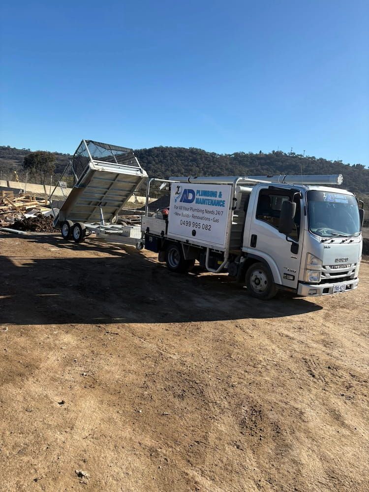 White Plumbing Service Truck With Trailer in a Dirt Field — AD Plumbing & Maintenance in Nicholls, ACT