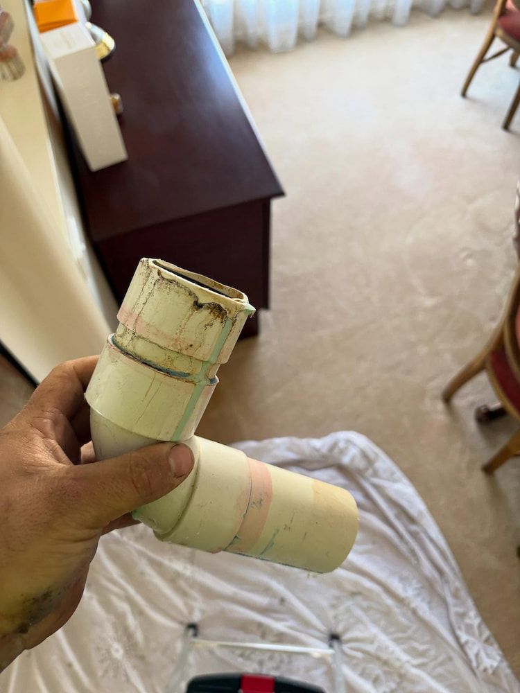 Hand Holding a White Pvc Pipe Elbow, Possibly for Plumbing Repair — AD Plumbing & Maintenance in Nicholls, ACT