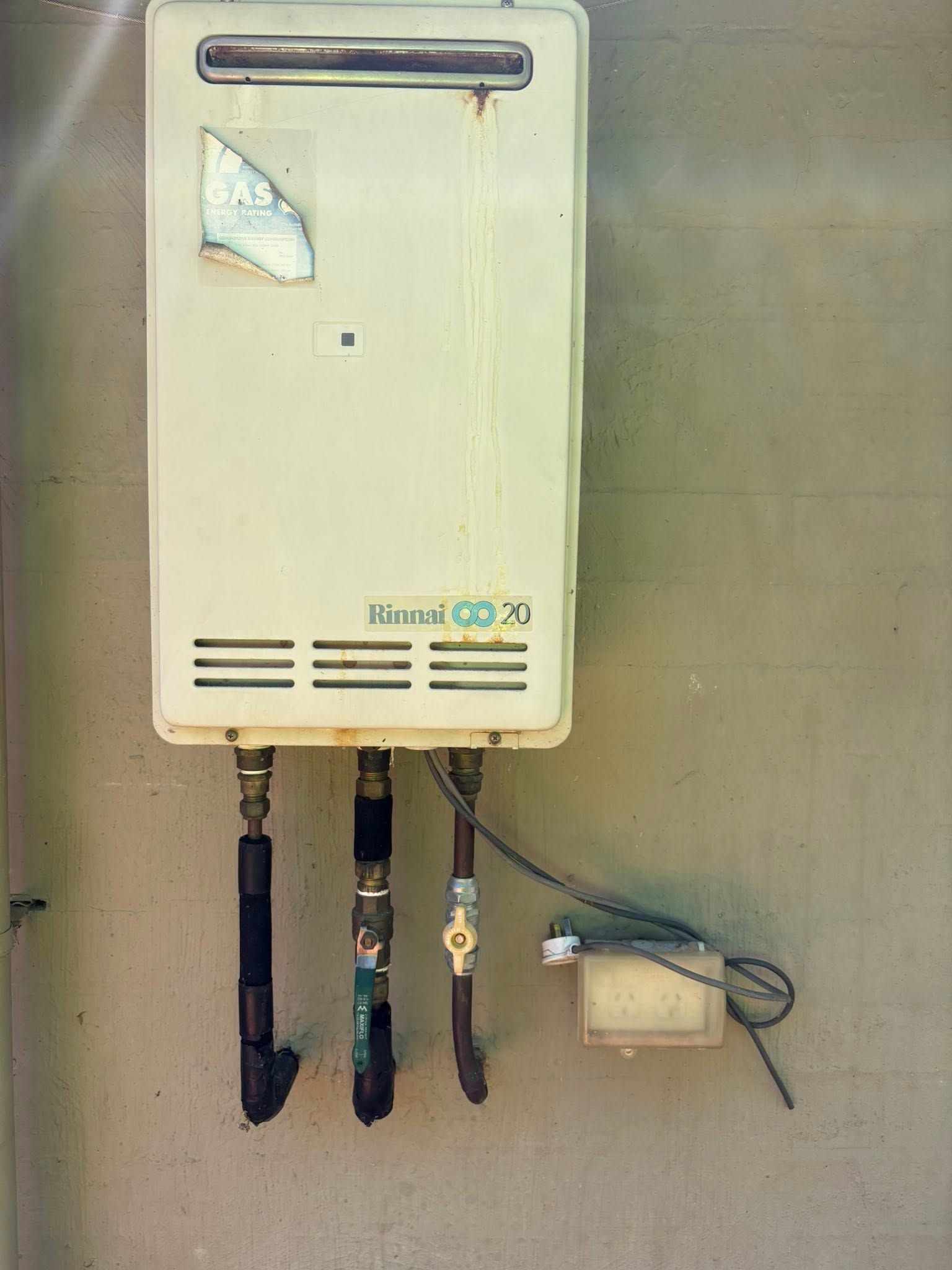 Wall-mounted Gas Water Heater With Exposed Pipes and Wiring Against a Tiled Wall — AD Plumbing & Maintenance in Canberra, ACT