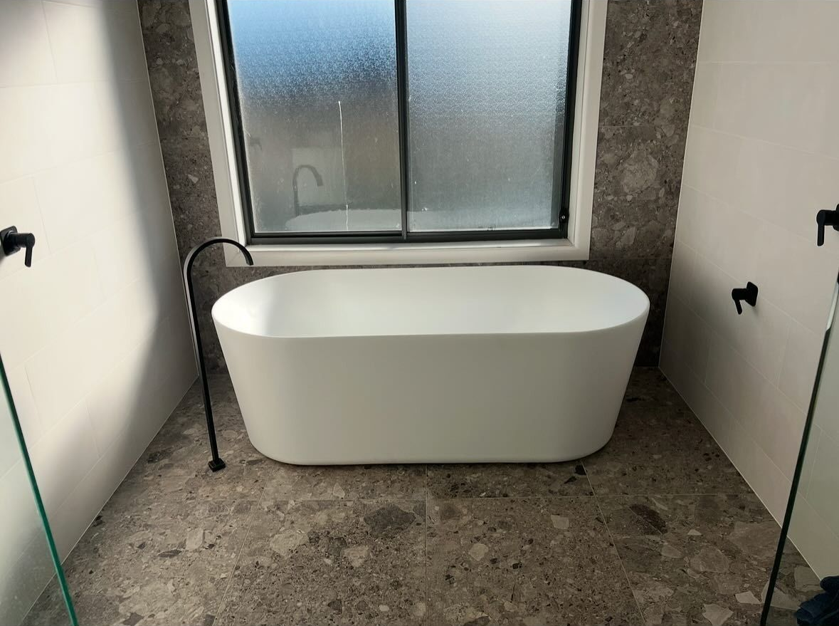 Bathroom With Freestanding White Tub Beneath Window and Stone Tile Floor — AD Plumbing & Maintenance in Canberra, ACT