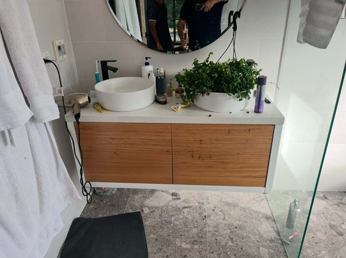 Bathroom Vanity With Mirror, White Sink, Wooden Cabinet, and a Potted Plant — AD Plumbing & Maintenance in Canberra, ACT