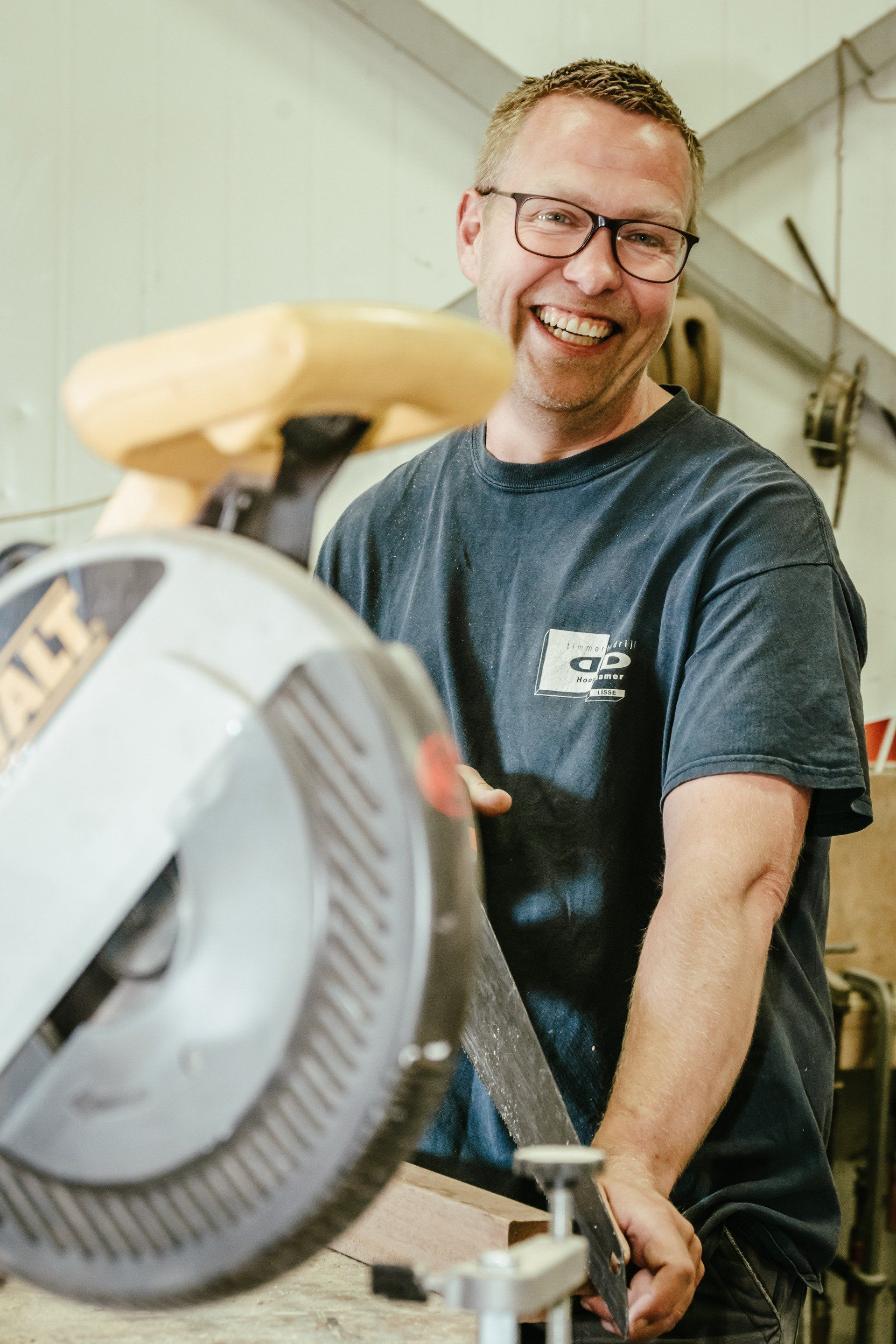 Een man lacht terwijl hij een stuk hout zaagt met een cirkelzaag. Portretten  M-stand fotografie