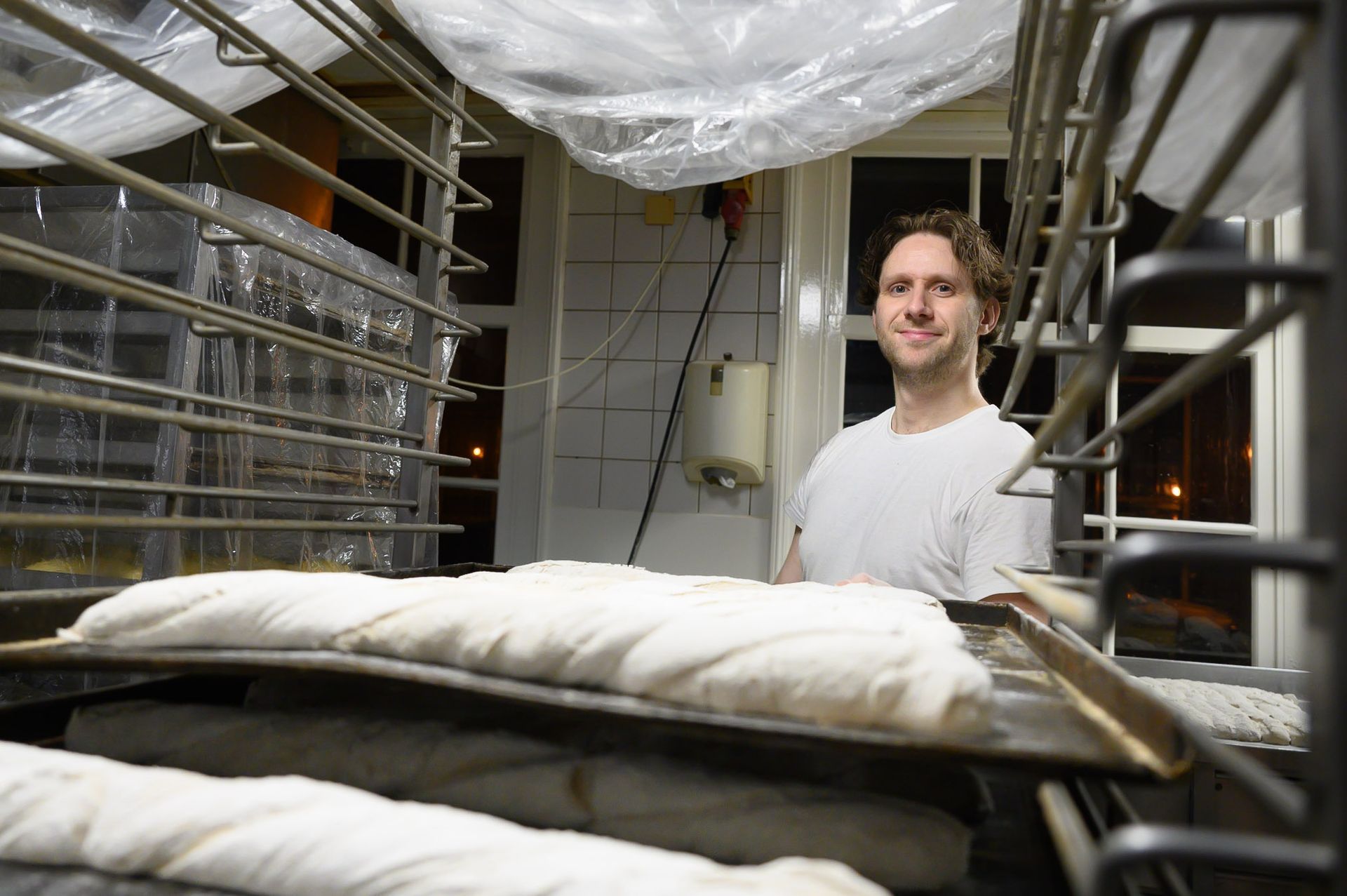 Een man staat naast een schaal met deeg in een bakkerij. Portretten  M-stand fotografie