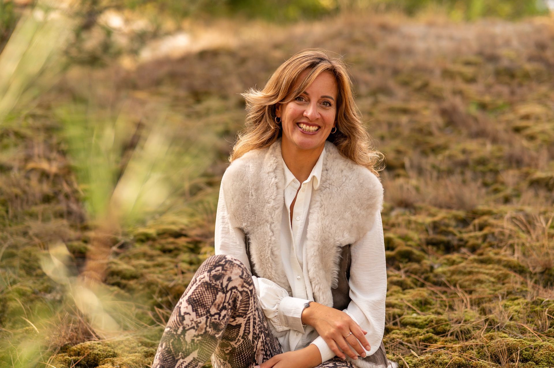 Een vrouw zit op de grond in een veld en draagt ​​een bontvest. M-stand fotografie