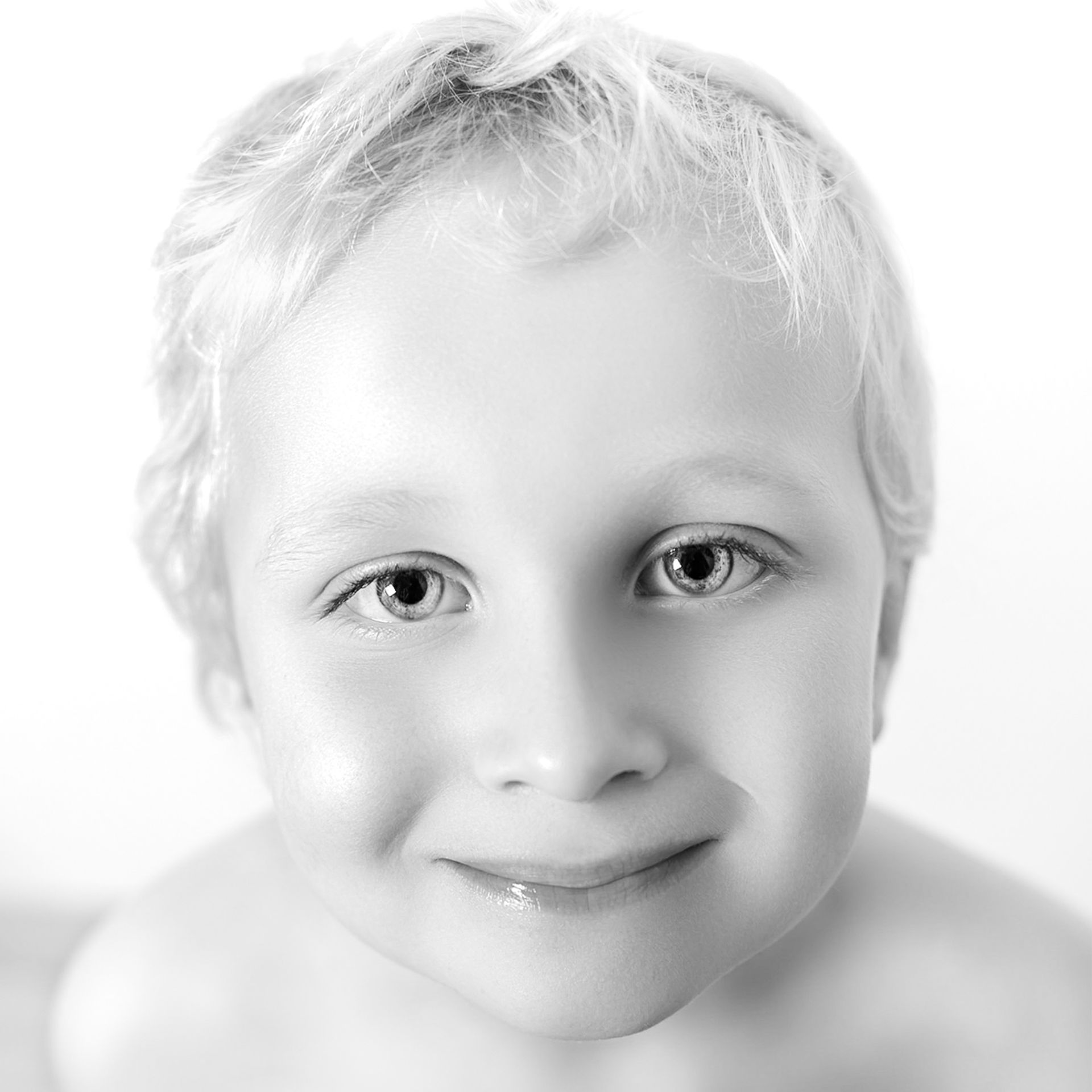 Een jonge jongen met blond haar lacht op een zwart-witfoto. Portretten  M-stand fotografie