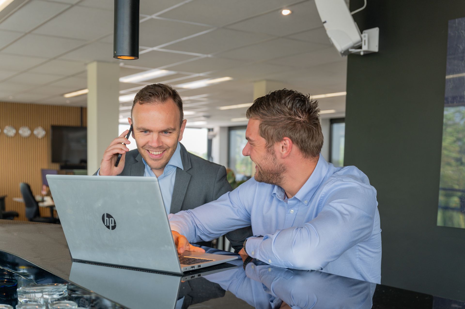 Twee mannen zitten aan een tafel en kijken naar een laptop. M-stand fotografie