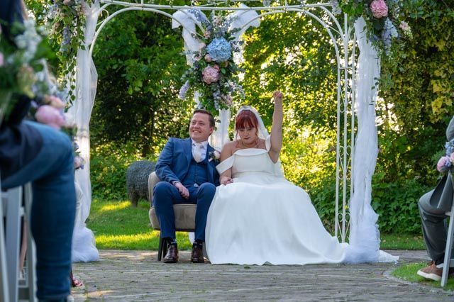 Een bruid en bruidegom zitten onder een boog tijdens hun huwelijksceremonie. M-stand fotografie