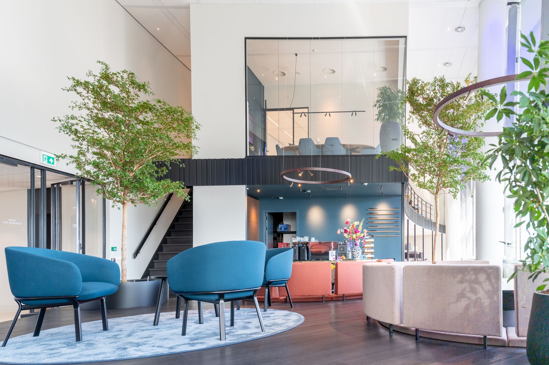 Een woonkamer met blauwe stoelen, tafels en bomen.