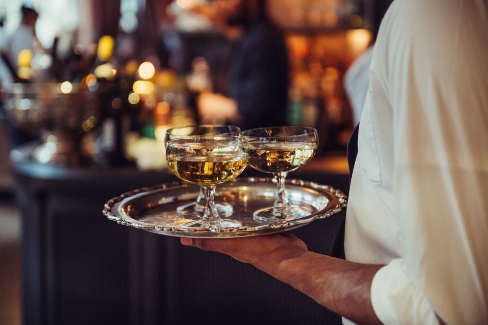 a waiter is holding a silver tray with two champagne glasses on it .