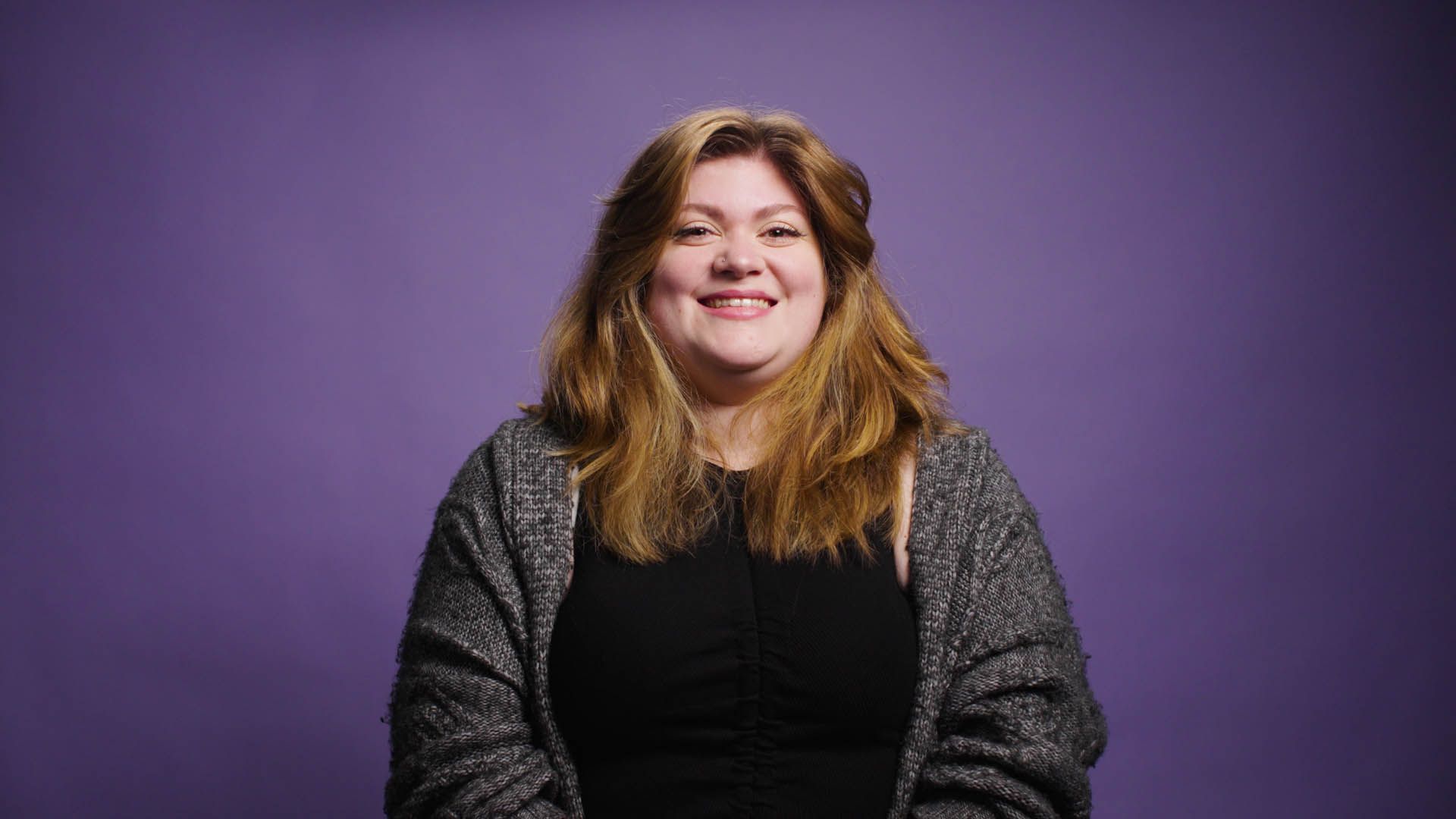 A woman is smiling in front of a purple background.
