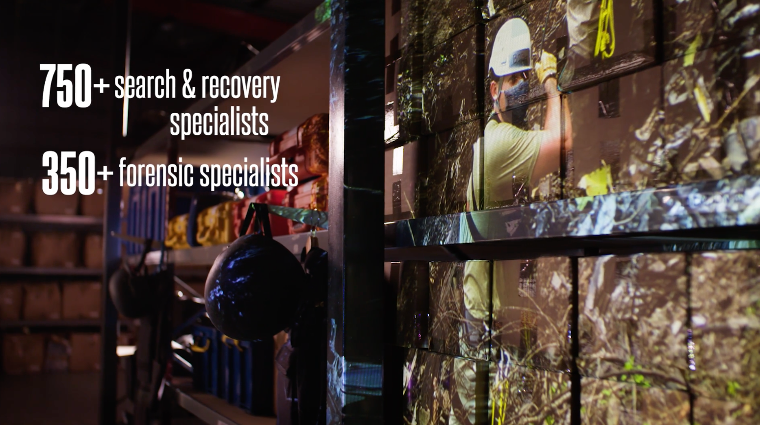 A man wearing a mask is working in a warehouse with 750+ search and recovery specialists and 350+ forensic specialists.
