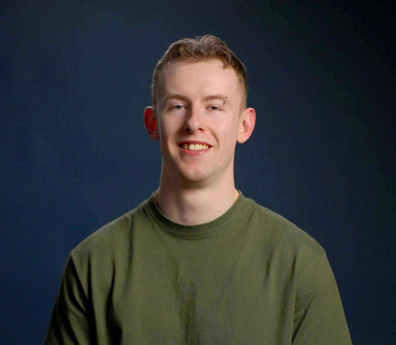 A young man wearing a striped shirt is smiling in front of a blue background.