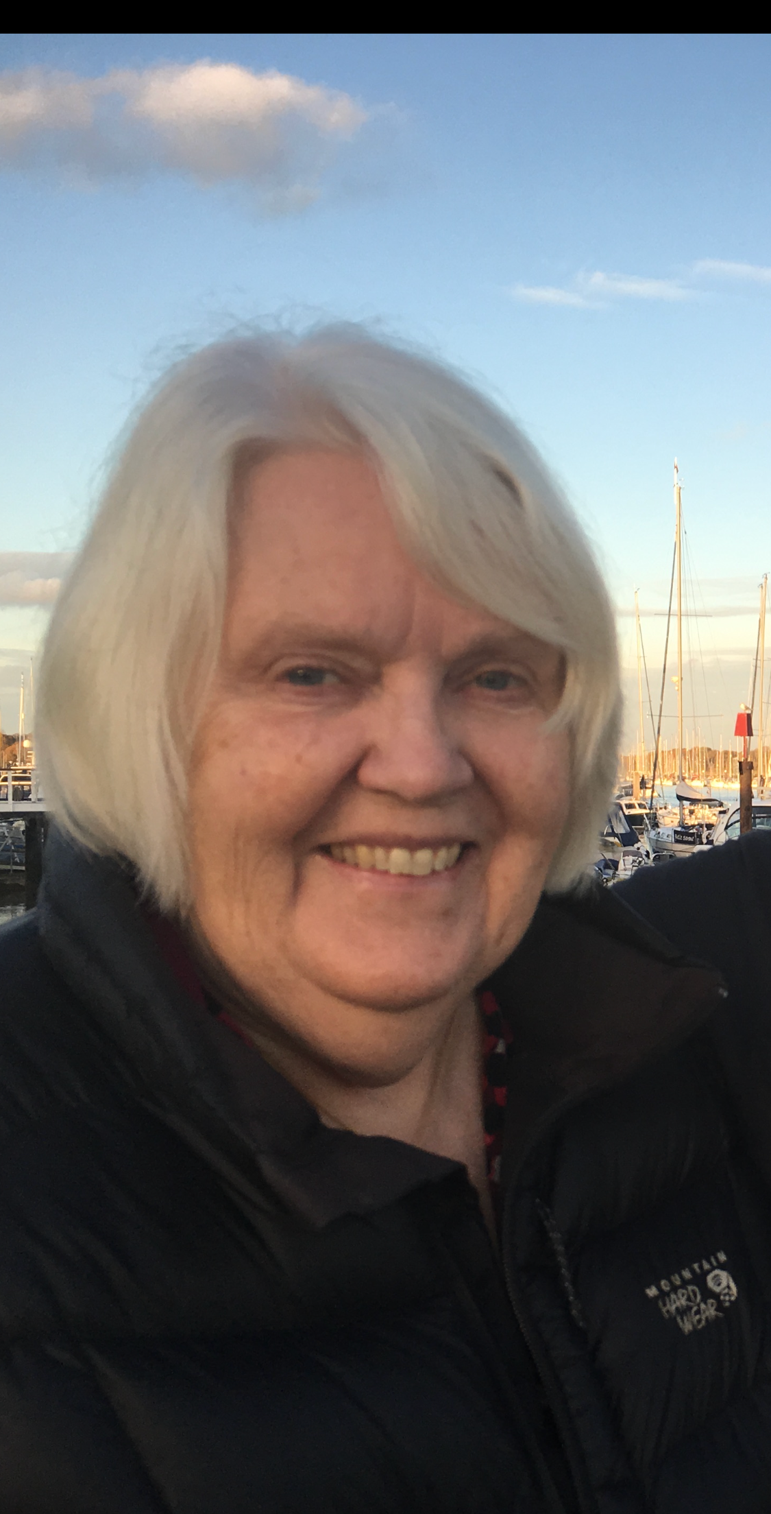 A woman with white hair is wearing a black jacket and smiling.