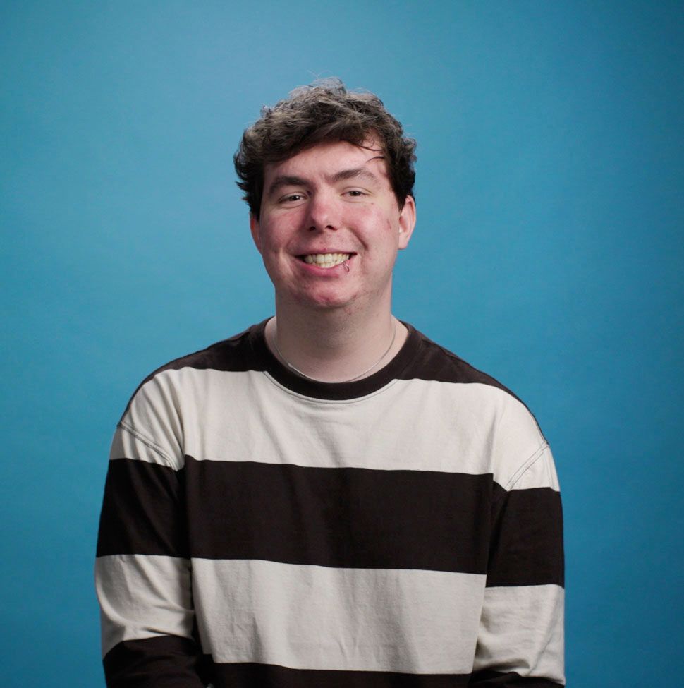 A young man wearing a striped shirt is smiling in front of a blue background.
