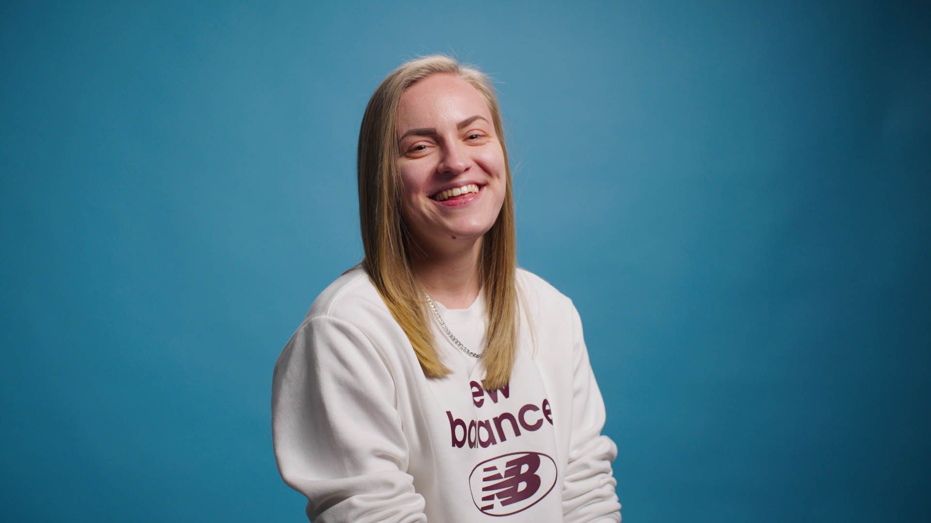 A woman wearing a white new balance sweatshirt is smiling.