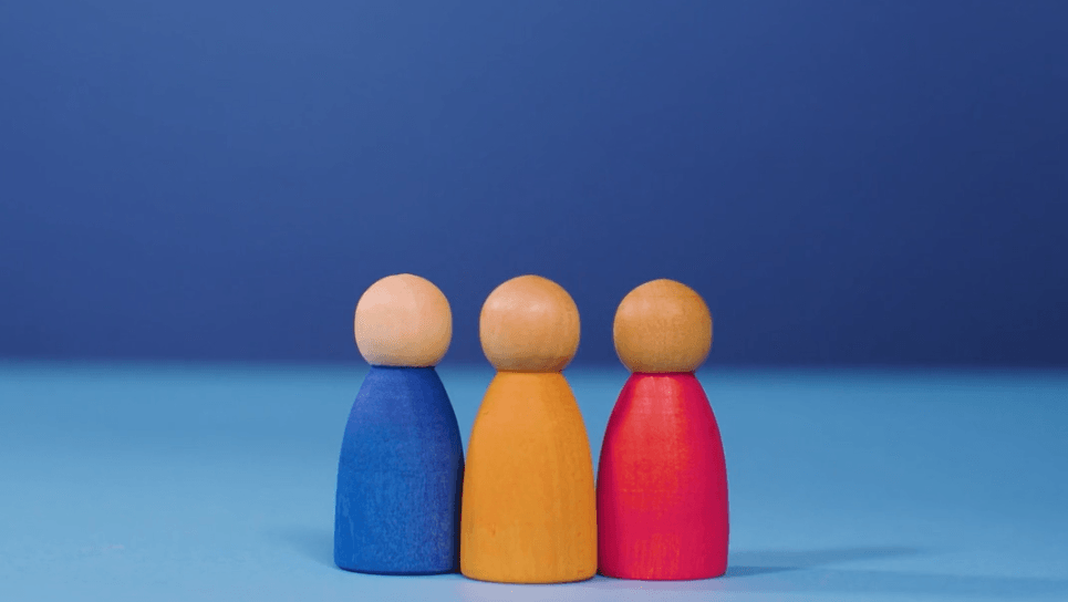 Three wooden dolls are standing next to each other on a blue table.