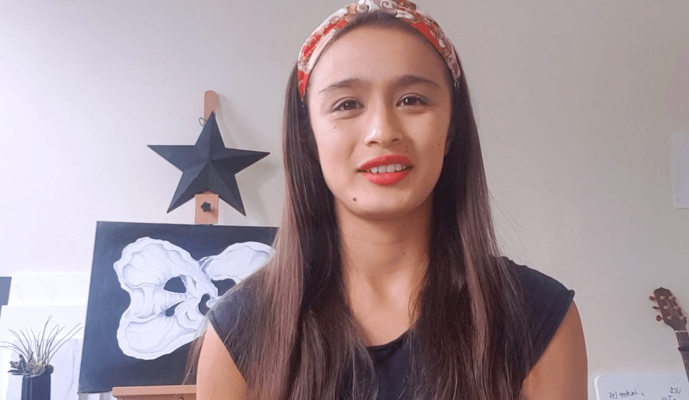 A woman wearing a headband is standing in front of a painting on an easel.