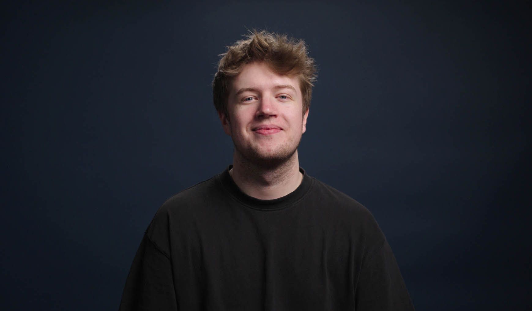 A young man in a black shirt is smiling and looking at the camera.