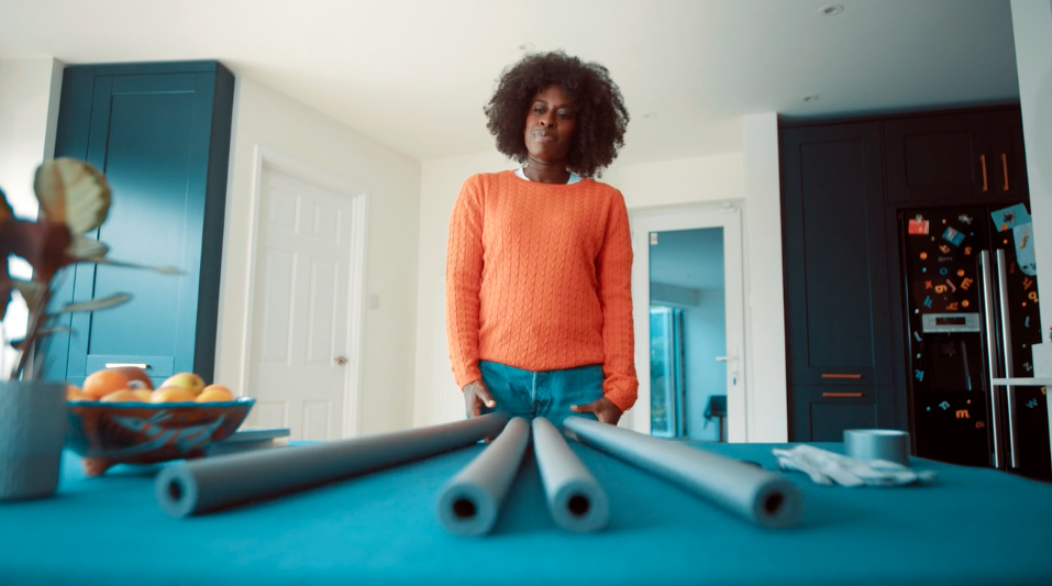 A woman in an orange sweater is standing next to a table with pipes on it.