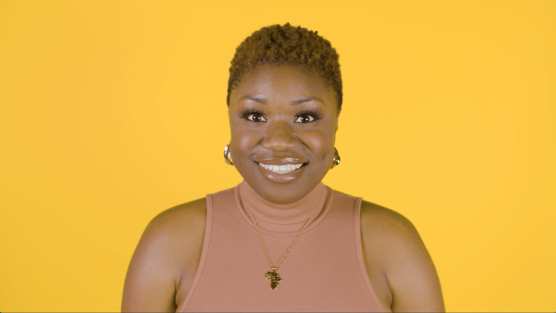 A woman in a pink tank top is smiling on a yellow background.