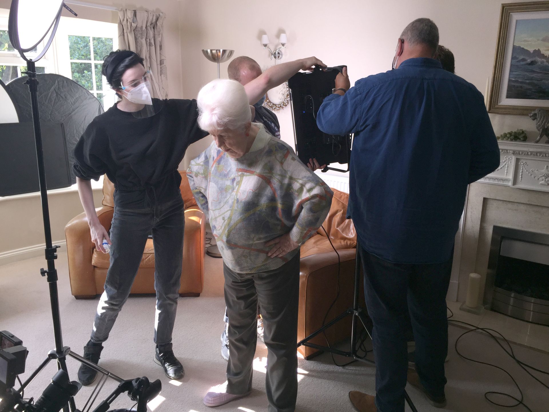 A group of people are standing around an older woman in a living room.