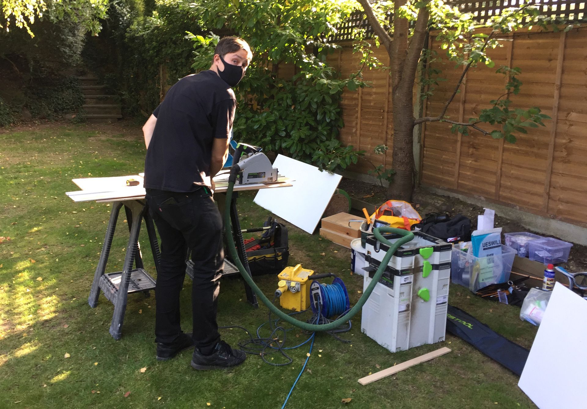 A man wearing a mask is using a circular saw in a backyard.