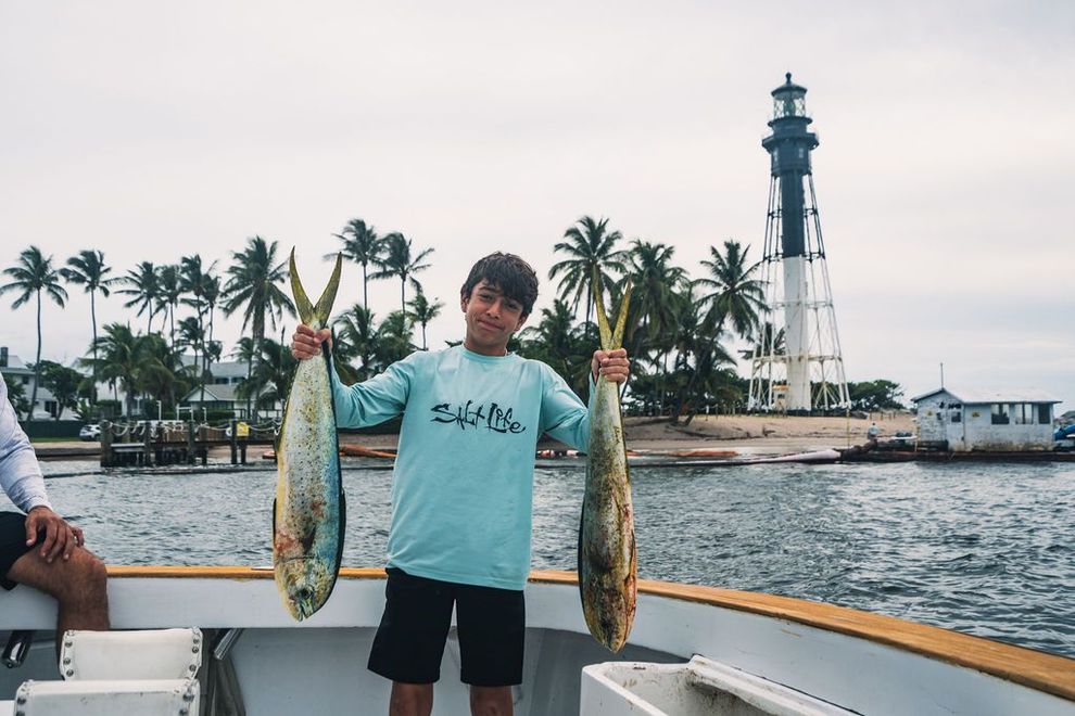 A young boy is holding two fish on a boat.