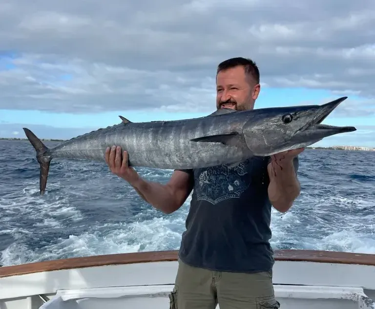 A man is holding a large fish on a boat in the ocean.