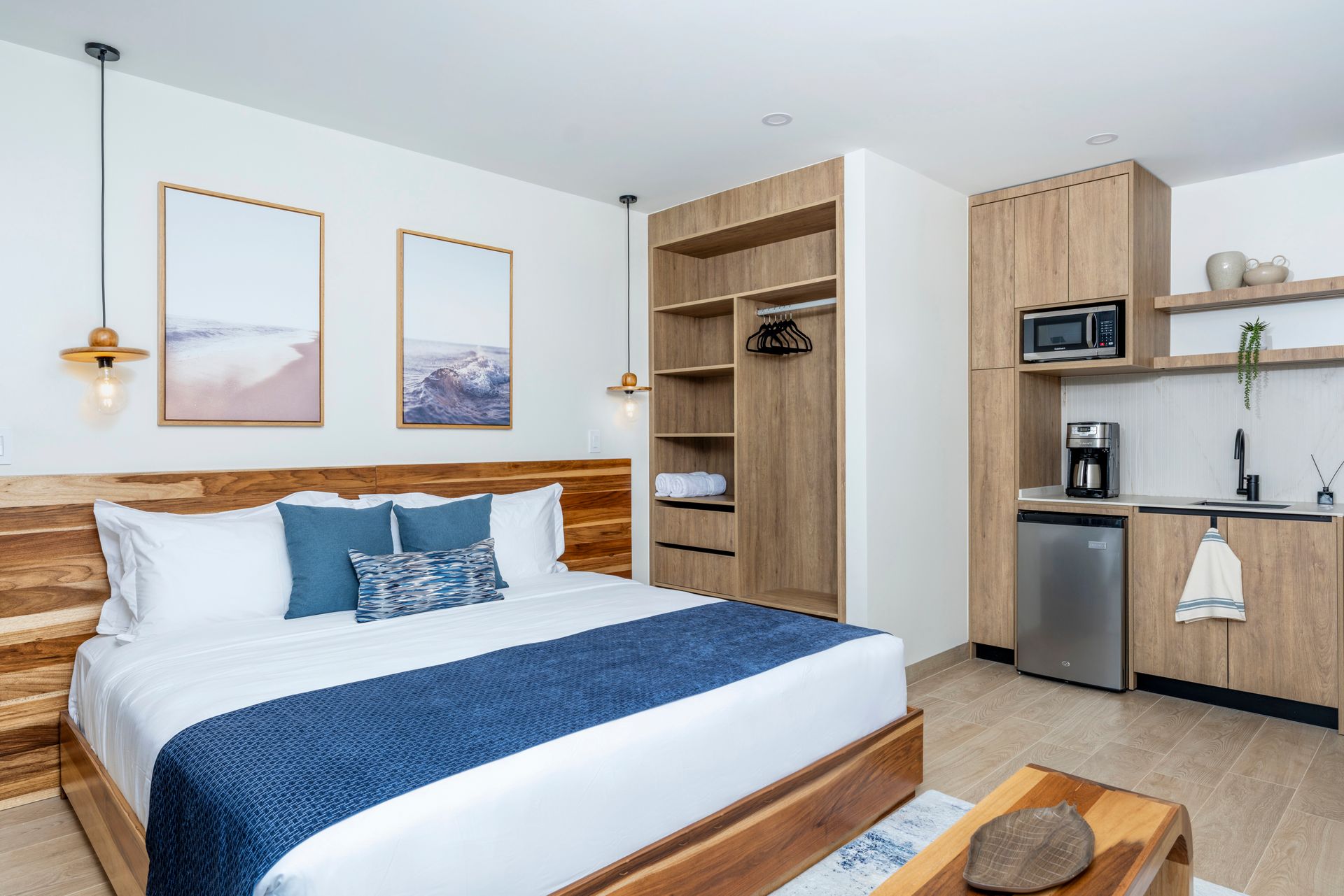 Modern bedroom with a bed, blue accents, wall art, and a small kitchenette area