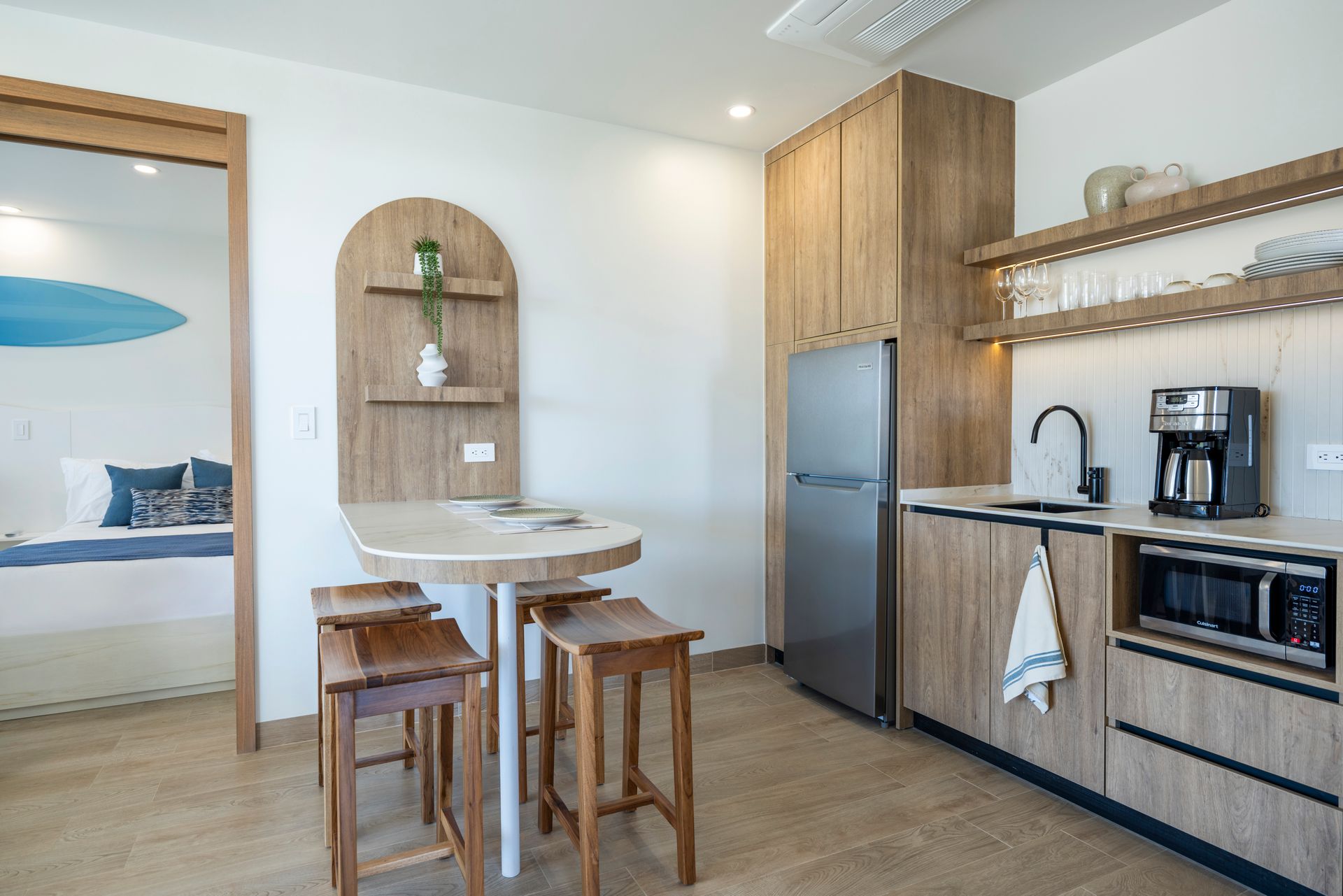 Modern kitchen and dining nook with wood cabinets, island stools, stainless fridge, and coffee machine