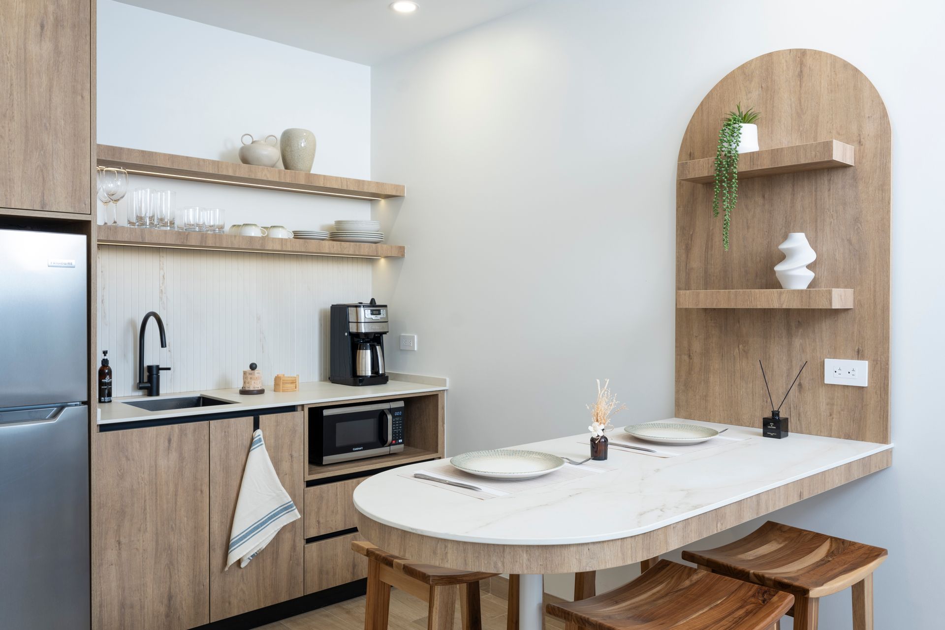 Modern kitchen and dining nook with light wood shelves, white table, and arched built-in shelving