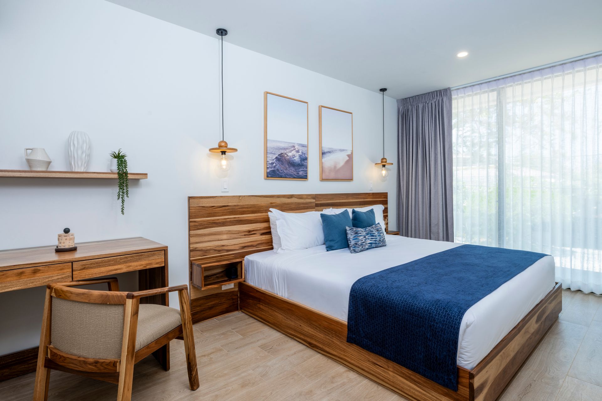 Modern bedroom with wood bed, blue bedding, desk, wall art, and bright window curtains