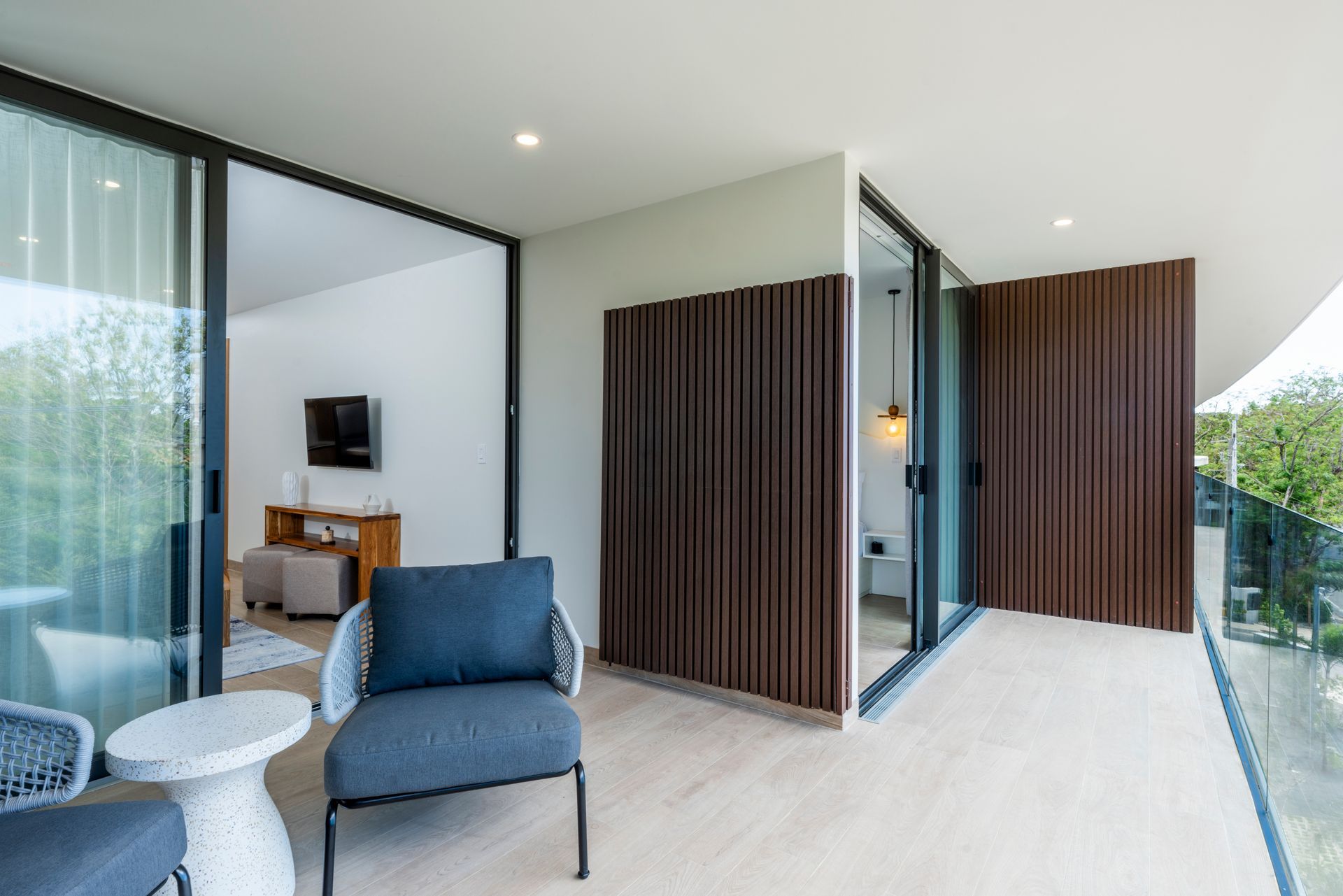 Modern outdoor patio with blue chairs, white table, glass walls, and slatted wood privacy screens