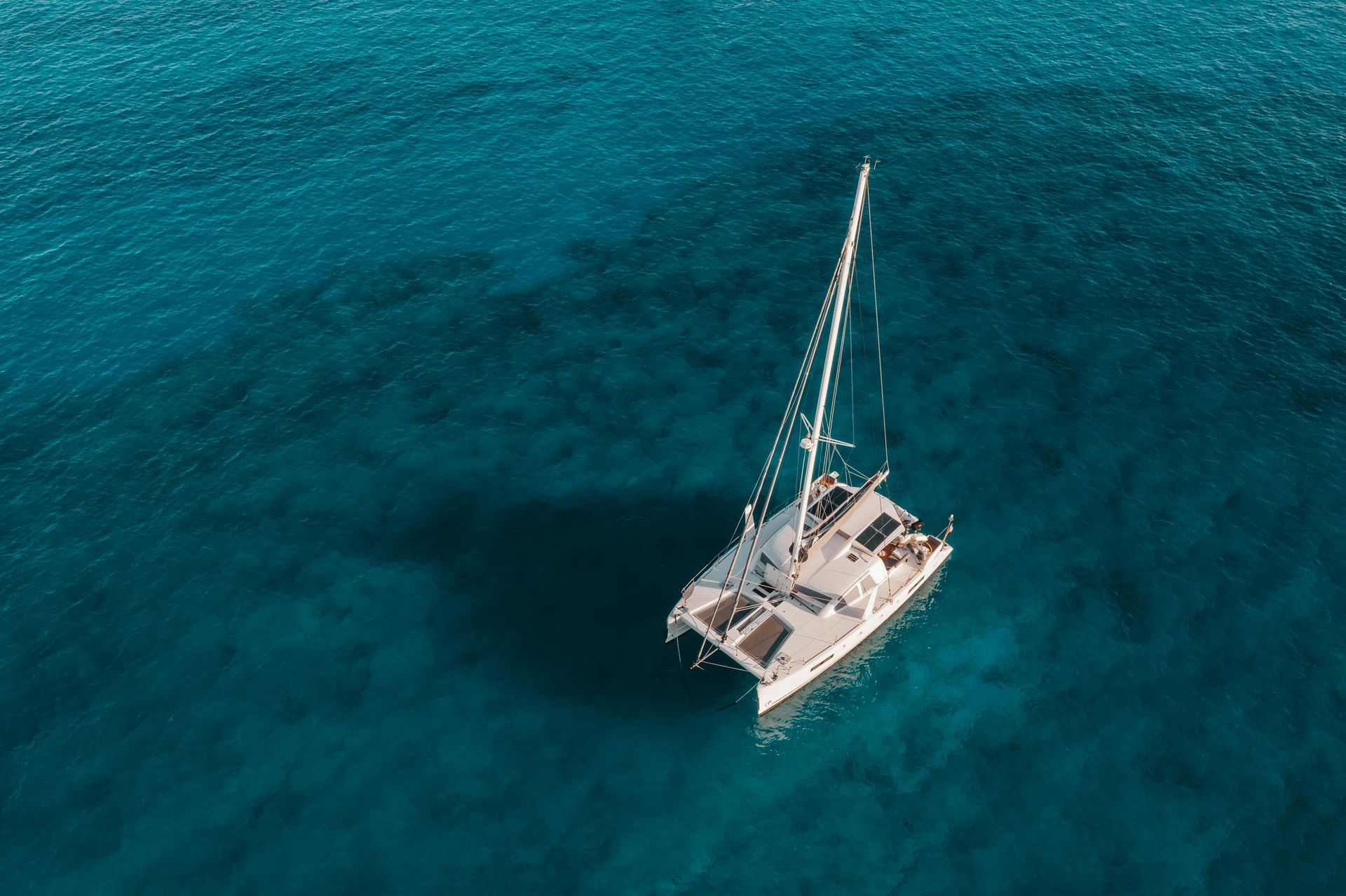 A white catamaran sailing on clear, turquoise water, with a shadow cast below.
