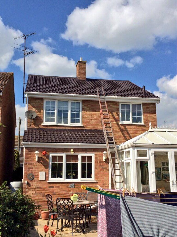 The back of a brick house with a ladder on the roof.