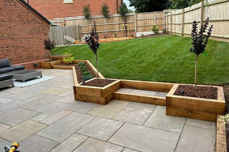 A patio with a wooden planter and a lawn in the background.