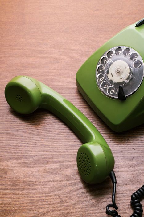 A green telephone is sitting on a wooden table next to another green telephone.