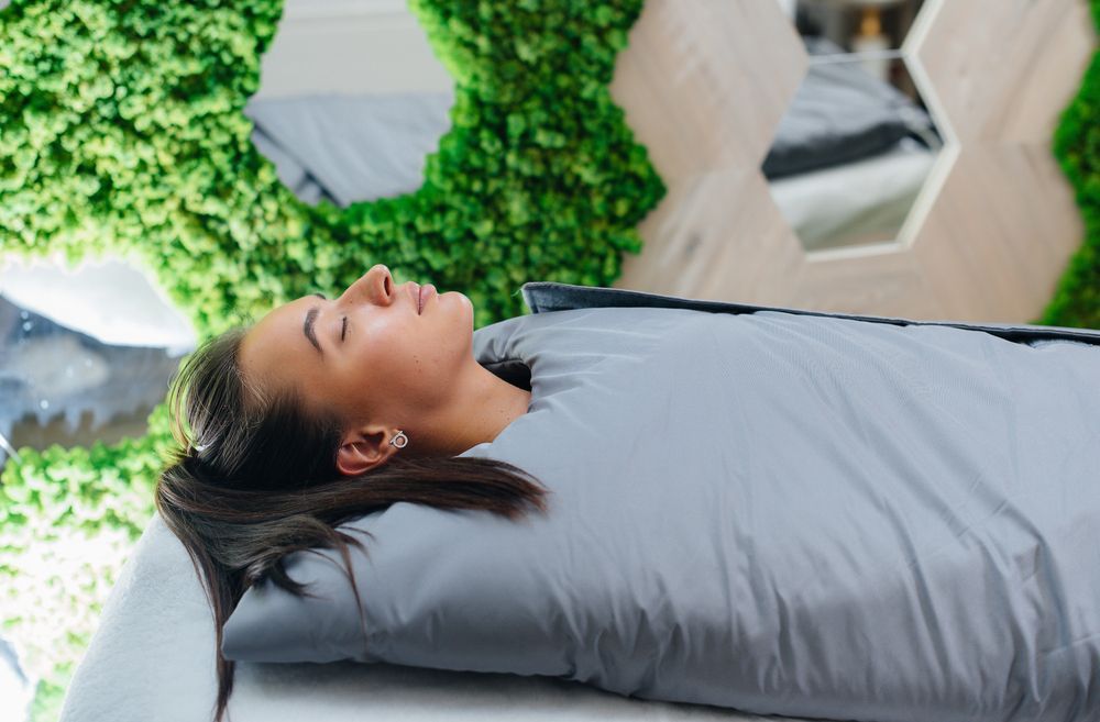 A woman is laying on a bed wrapped in a blanket.