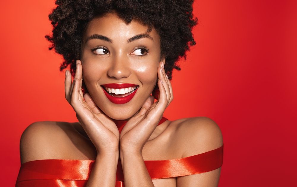 A woman is wrapped in a red ribbon and smiling.