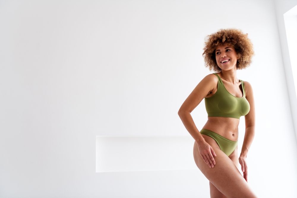 A woman in green underwear is standing in front of a white wall.