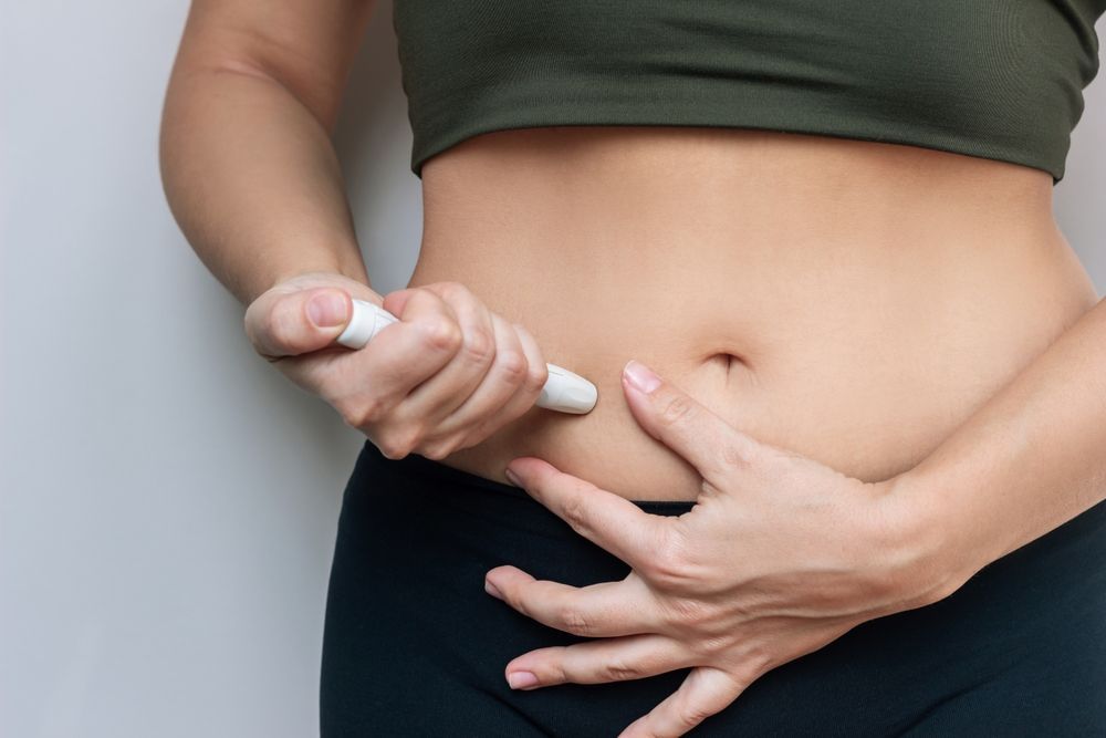 A woman is holding a syringe to her stomach.