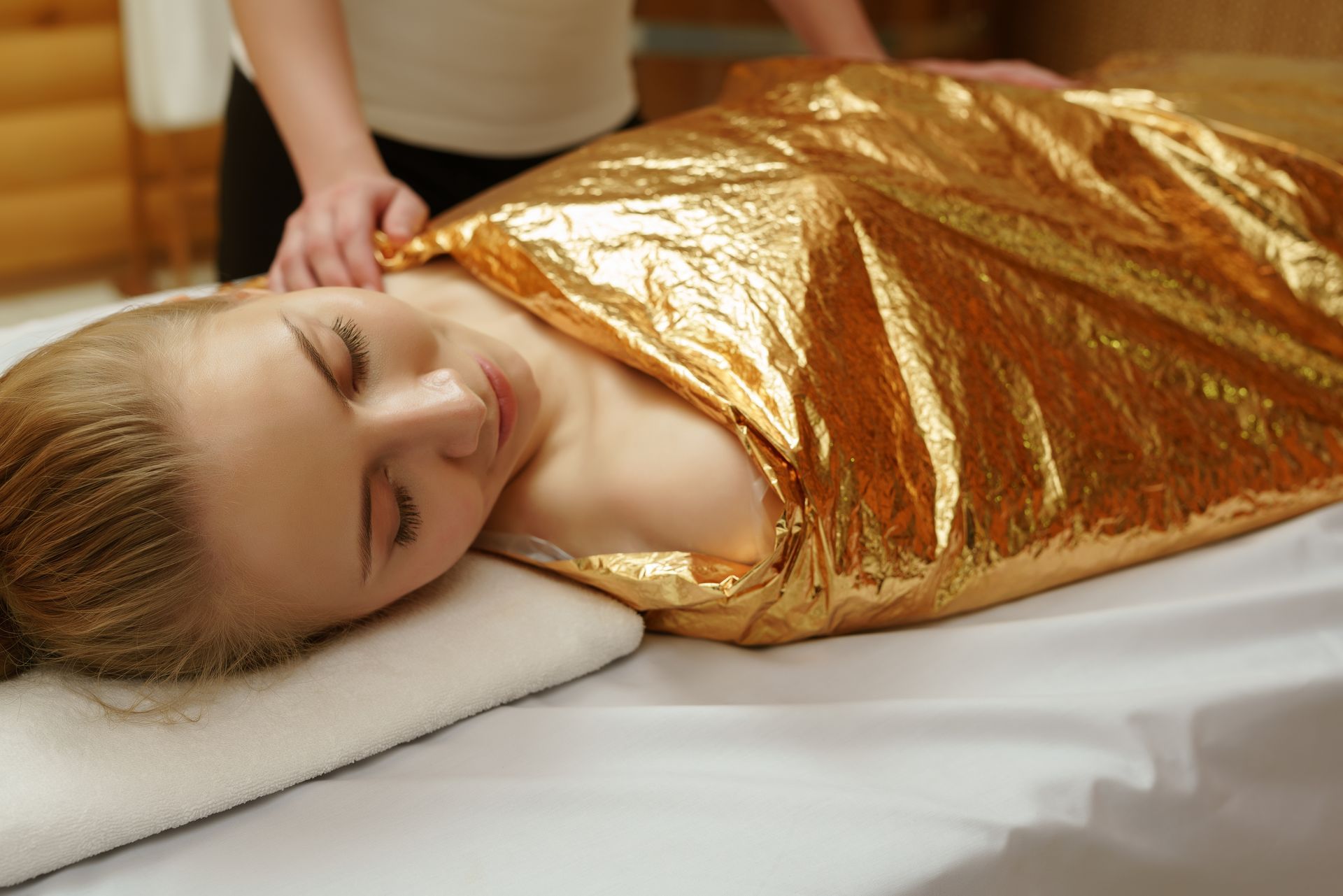 A woman is wrapped in a gold foil blanket at a spa.