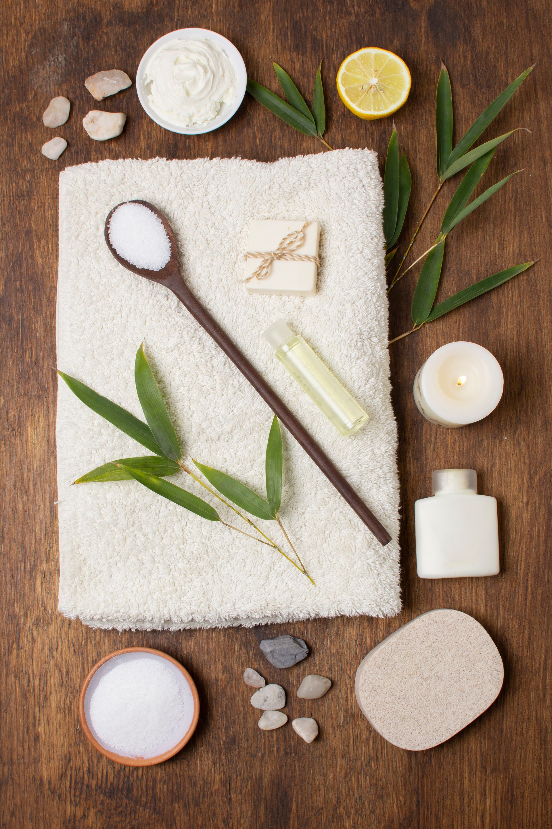 A wooden table topped with a towel , spoon , candles , leaves and other spa items.